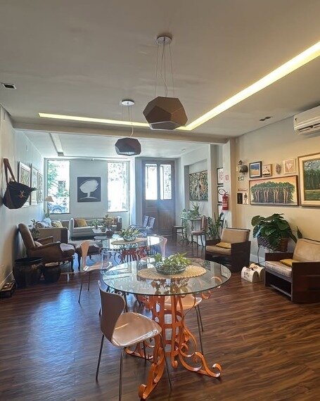 Sala de atendimento do escritório, com mesa de vidro, sofás e quadros na parede
